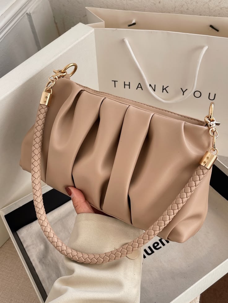 Beige handbag with braided handle held by a hand, with a 'THANK YOU' gift bag in the background.