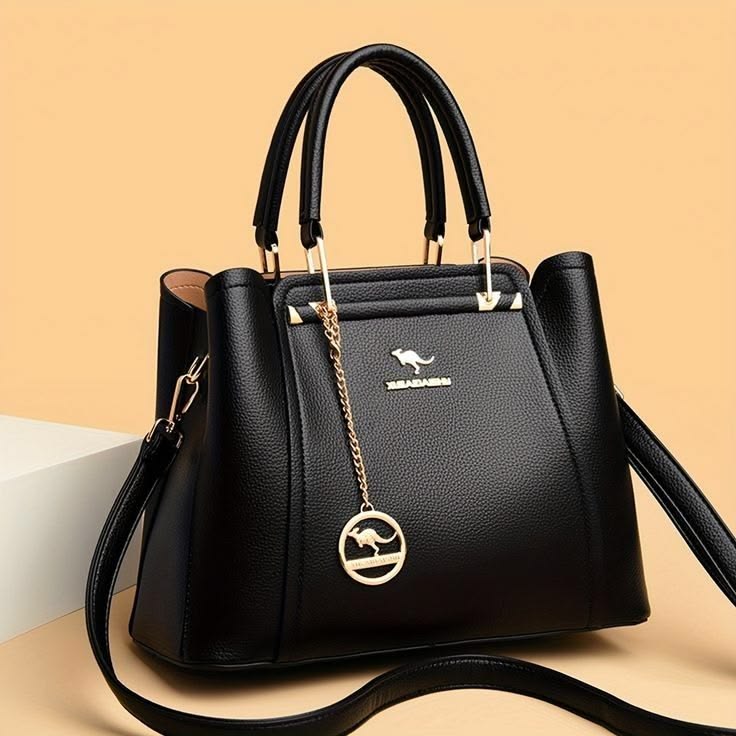 Black handbag with a gold chain and emblem on a beige background