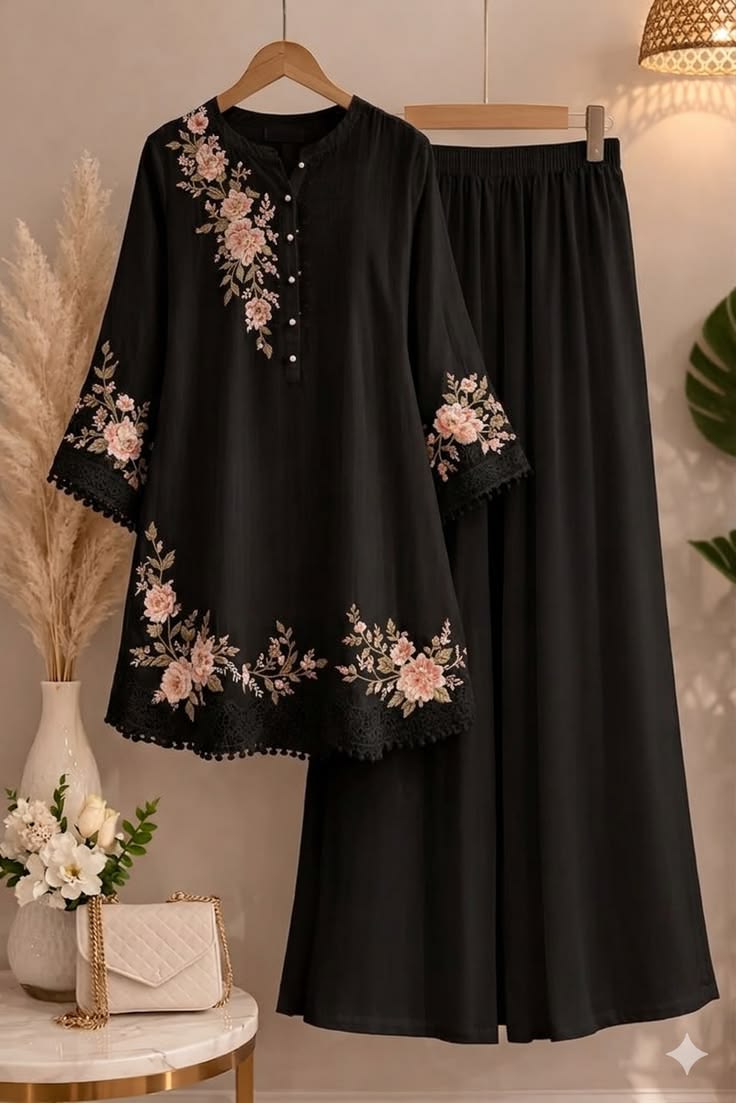 Black outfit with floral embroidery on a hanger against a neutral background