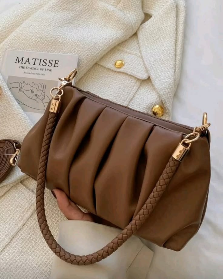 Brown handbag with braided handle held by a hand, with a beige textured background.