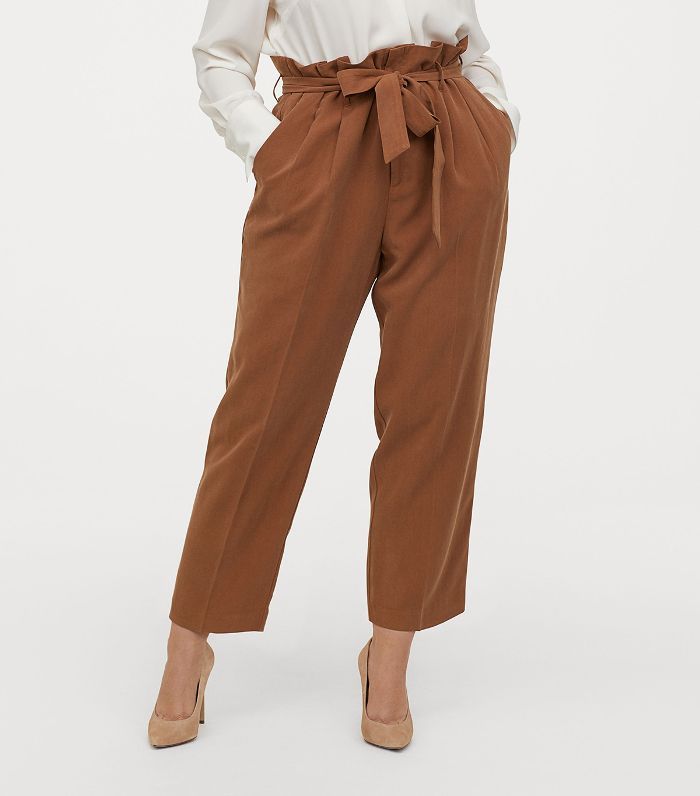Brown paperbag pants worn with a white shirt on a white background