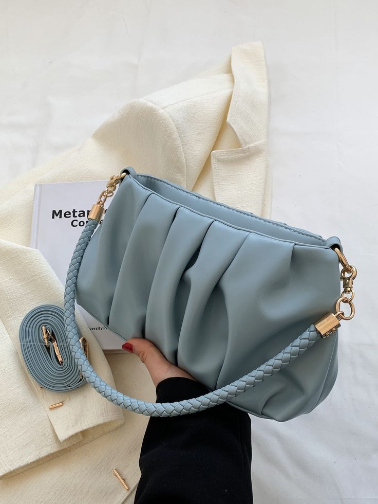 Light blue handbag with braided handle held by a hand on a white background