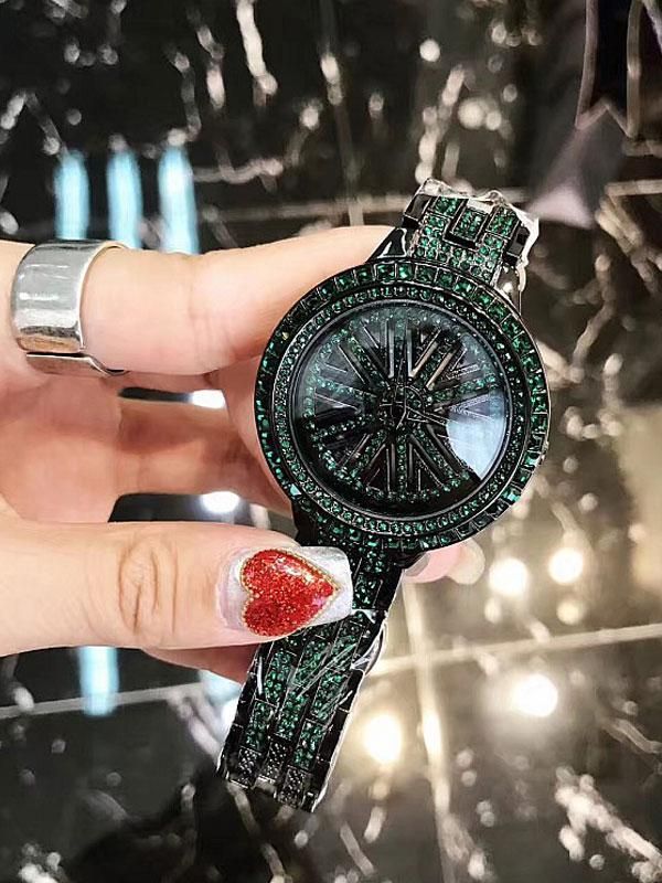 Luxury watch with green gemstones held by a hand against a reflective surface.