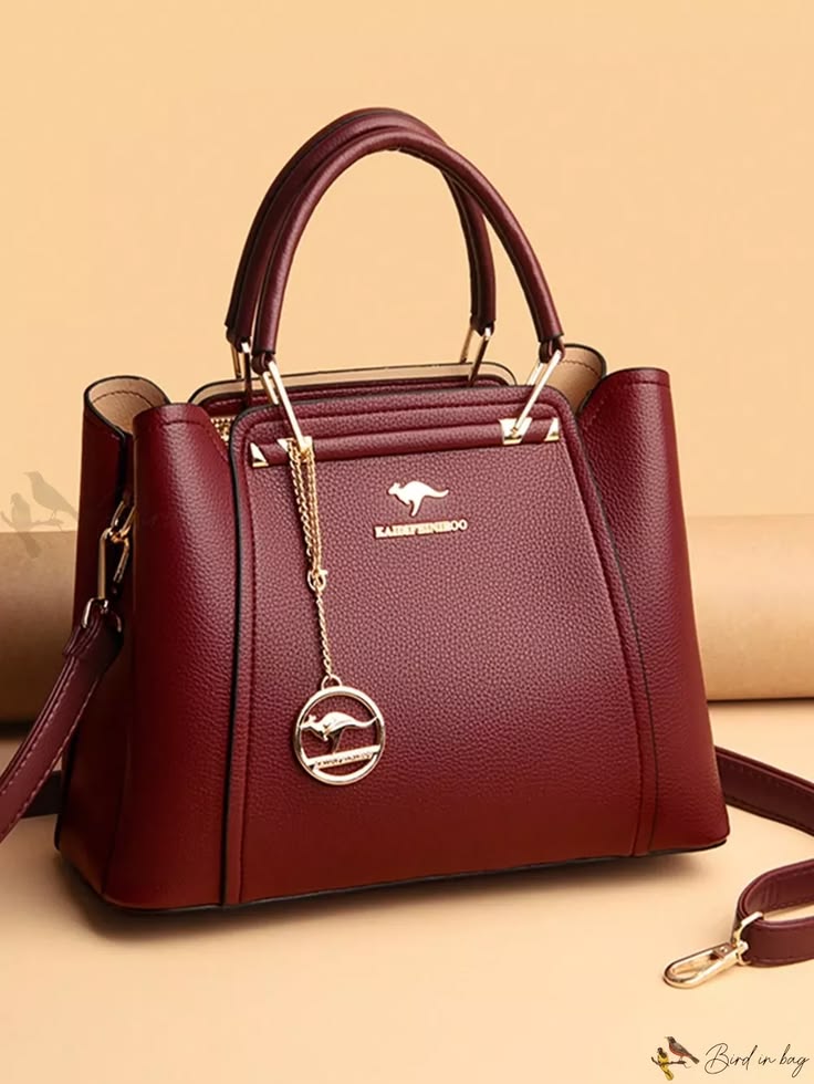 Maroon handbag with a brand logo on a beige background
