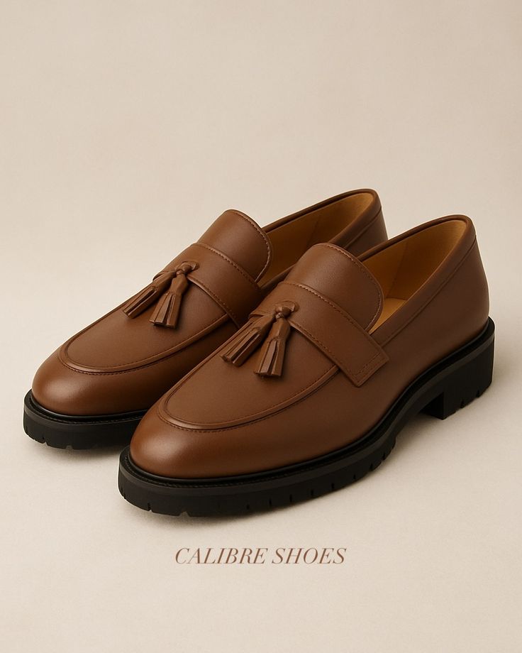 Pair of brown loafers with tassels on a beige background, branded 'Calibre Shoes'.