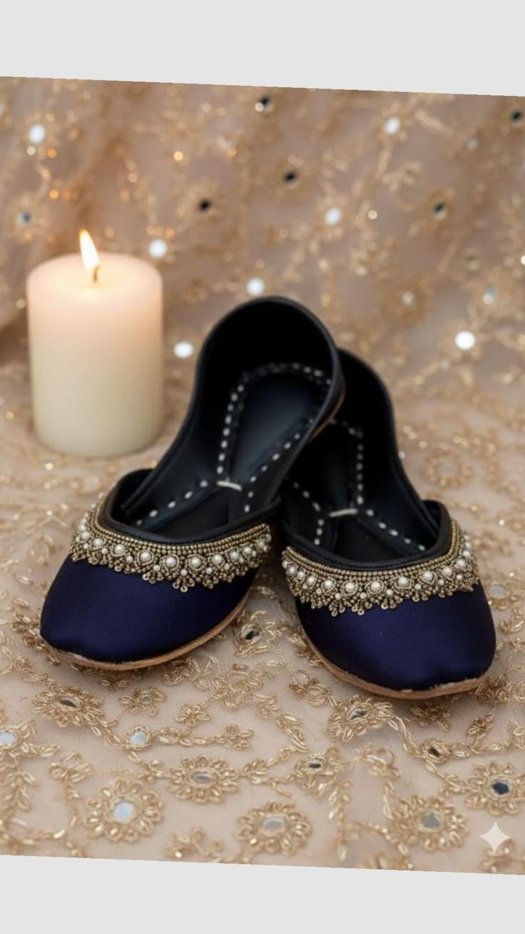 Pair of navy blue flats with gold embellishments on a decorative fabric background with a candle.