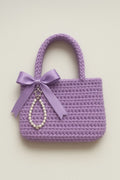 Purple crocheted handbag with a bow and decorative chain on a light background