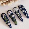 Set of four navy blue hair clips with floral designs on a light background